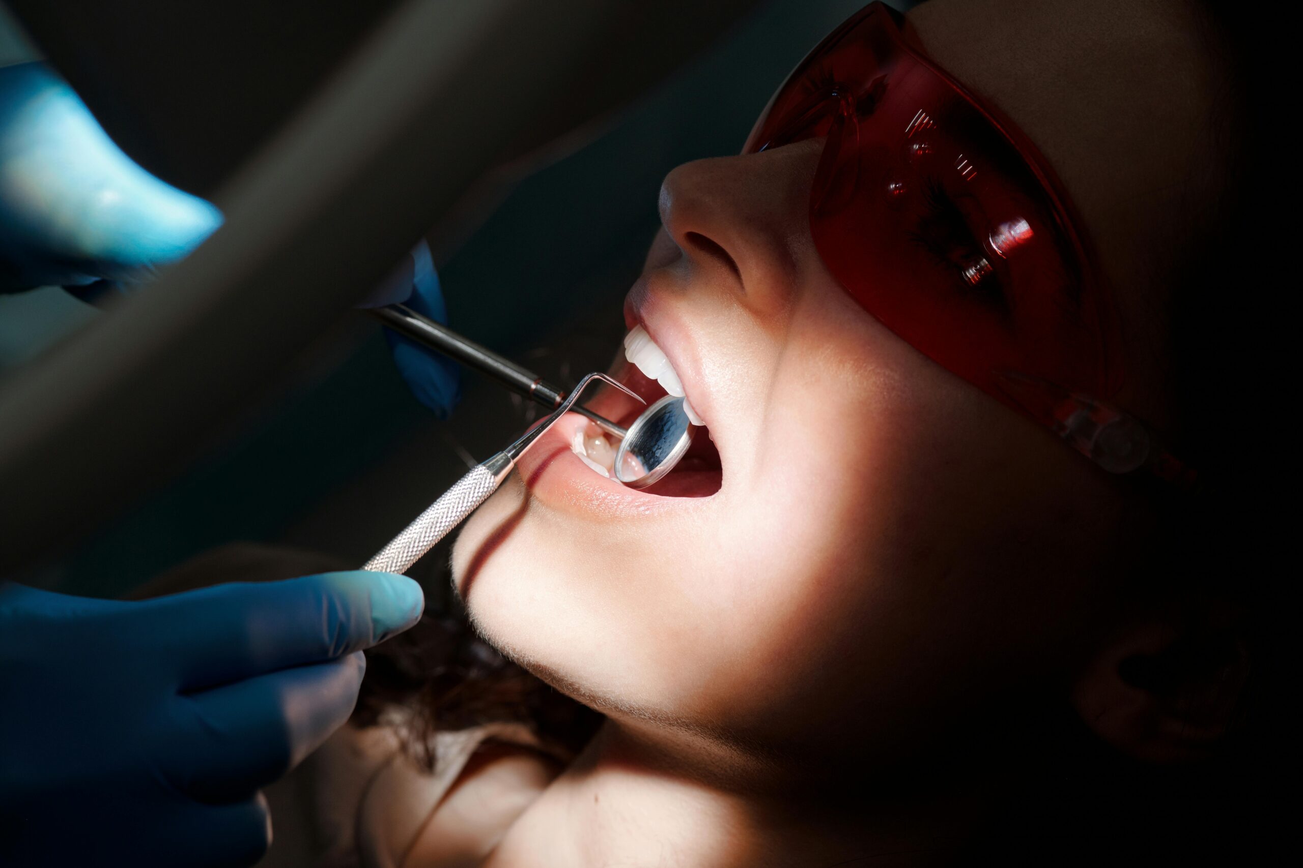 A detailed close-up of a dental examination showing tools and a patient with protective eyewear.